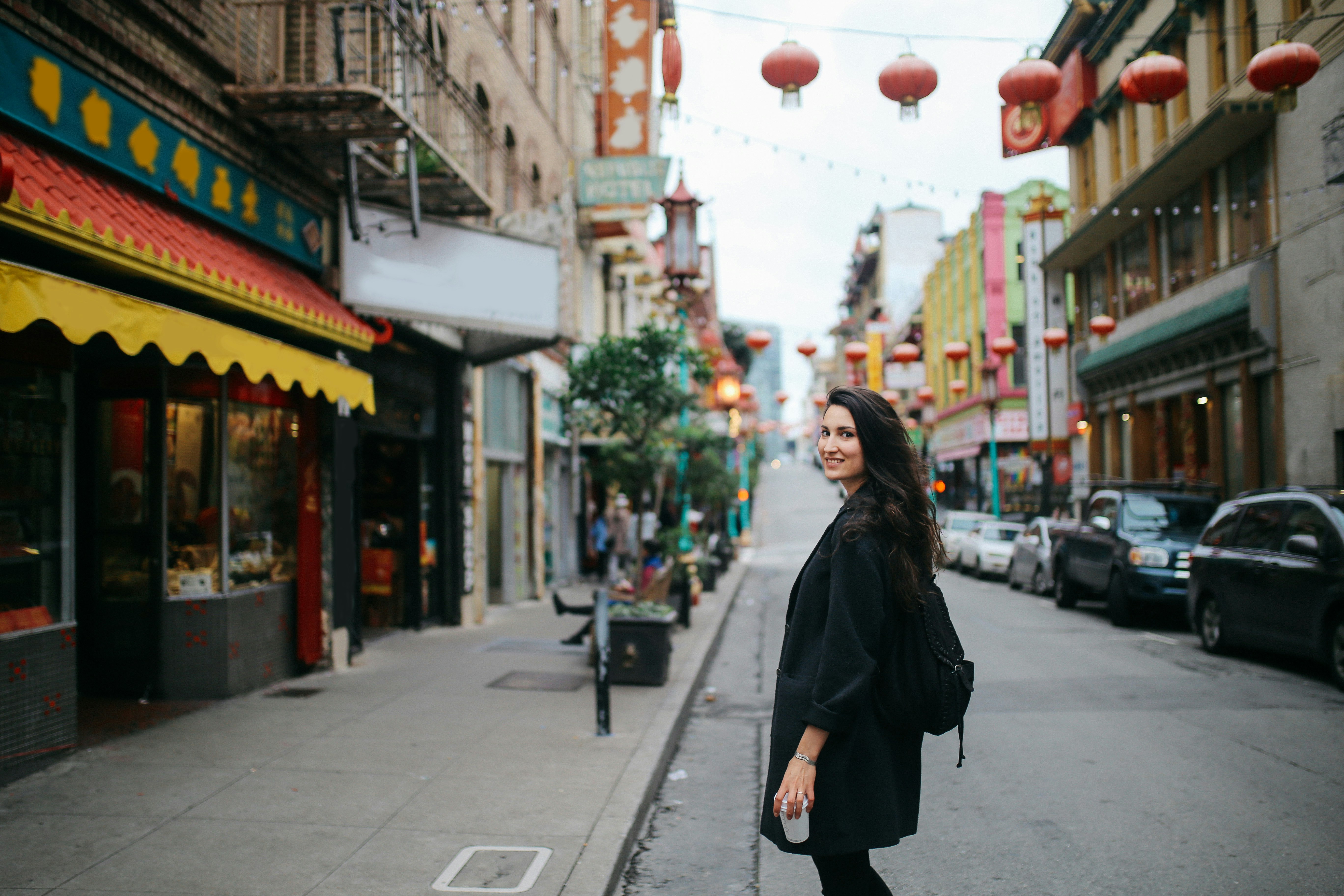 Young woman walking down the Chinatown district in San Francisco, California. She is wearing casual clothing, carrying a cup of coffee to go, enjoying the vibrant and famous Chinese district.